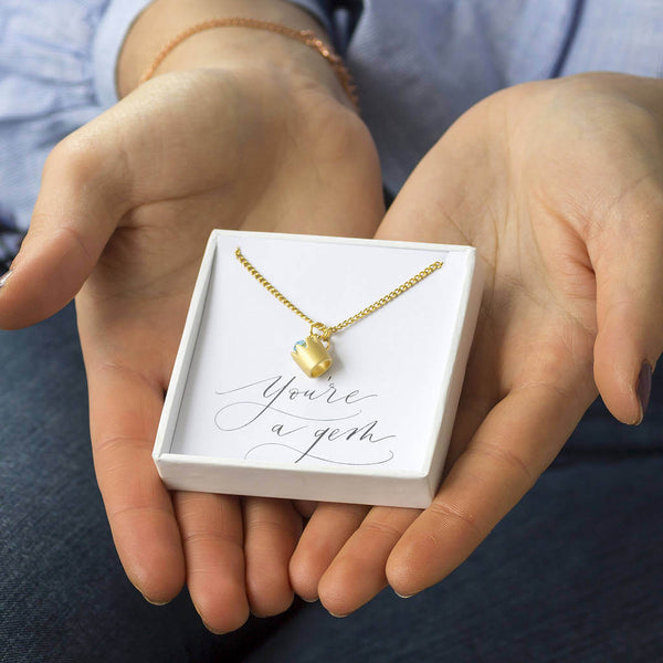 Image shows model holding Gold Crown Birthstone Necklace in a gift box on you're a gem sentiment card