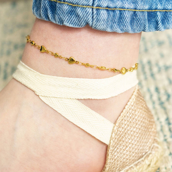 Model wears gold plated graduated hearts anklet and cream sandals.