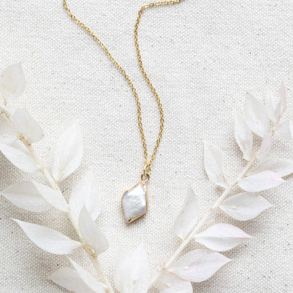 Gold rhombus pearl pendant necklace on a cream linen background