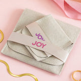 Image shows two suedette pouches in two sizes branded with 'JOY' on a pink backdrop.Image shows a joy by corrine smith branded suedette pouch