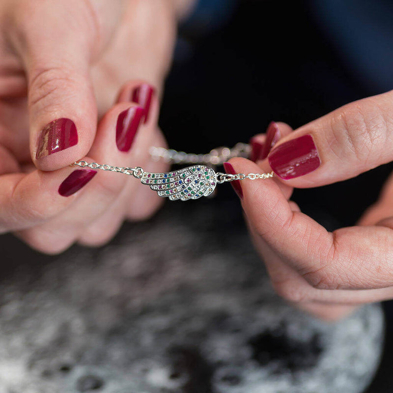 Image shows model holding silver micro pave multi coloured angel wing bracelet