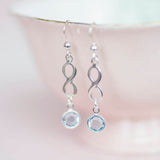 Image shows model wearing sterling silver infinity birthstone earrings with March birthstone