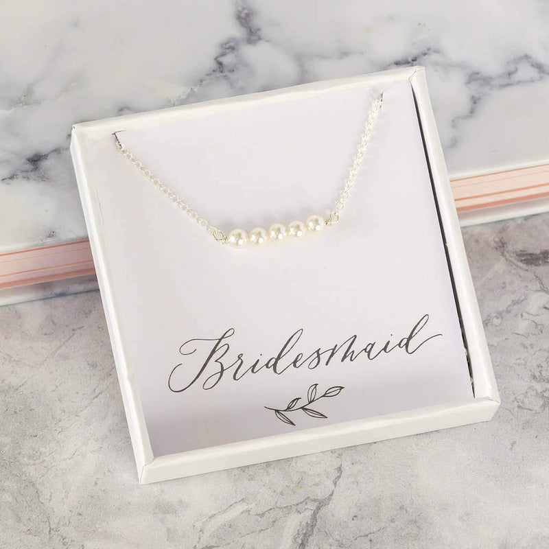 Silver delicate Swarovski pearl necklace sits in the box on the bridesmaid sentiment card