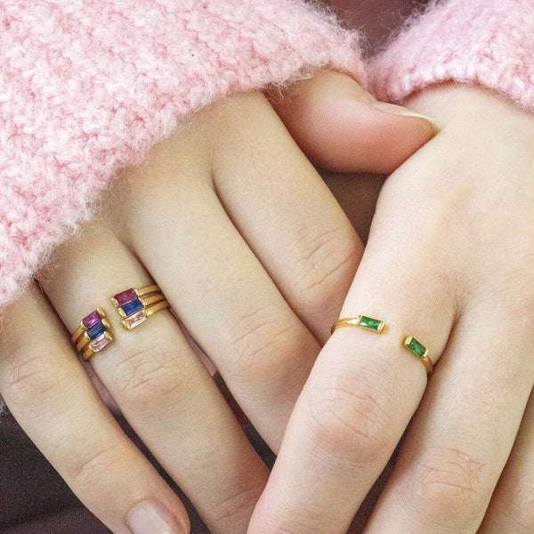 Model wears three Baguette Birthstone Stacking Rings on the left and a single May Emerald Baguette Birthstone Stacking Ring on the right.