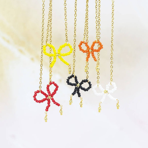 Image shows five handmade beaded bow necklaces in white, yellow, orange, black and red on a pals background