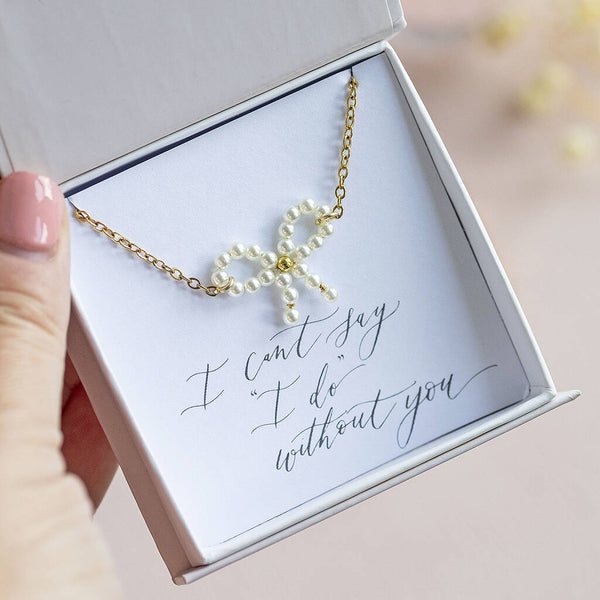 Image shows gold plated Bridesmaid Pearl Bow Necklace on an "I can't say 'I do' without you" sentiment card in a JOY by Corrine Smith gift box.