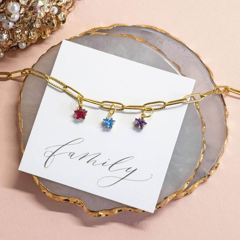 Image shows Gold Plated Family Birthstone Stars Bracelet with July, March and February birthstones. Bracelet is on a 'family' sentiment card on a pink backdrop.
