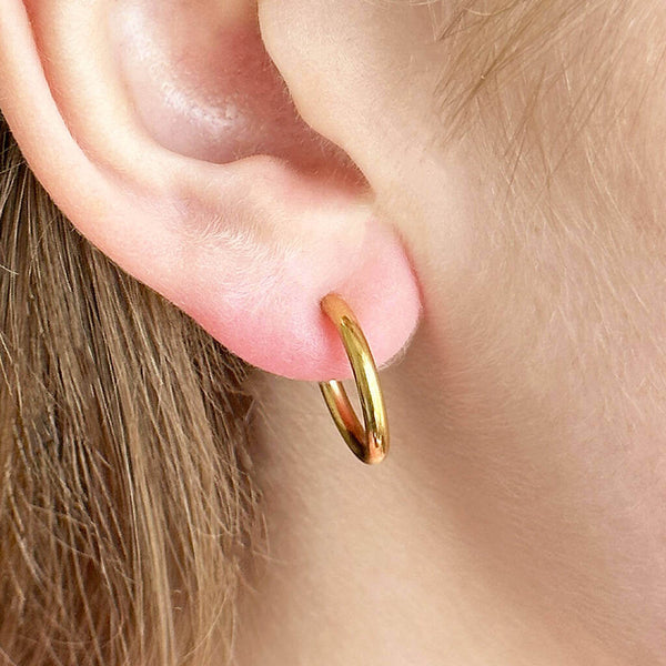 Gold plated huggie hoop earring worn on woman's ear