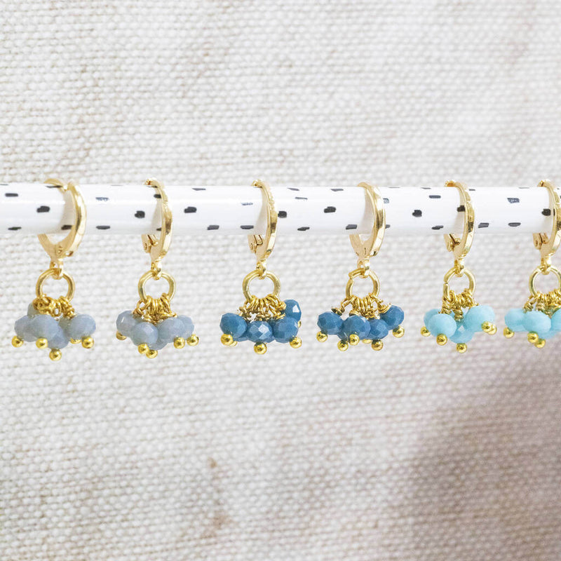 Image shows all three colours of Shades of Blue Huggie Hoop Charm Earrings from left: grey-light blue, indigo and turquoise.