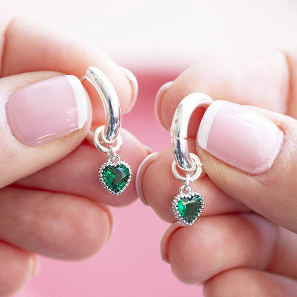 Silver plated huggie hoop earrings with the emerald May birthstone hearts been held 