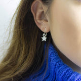 Silver star earrings worn by woman with long dark hair and a blue chunky knit jumper.