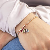 Model wears family marquise style birthstone bracelet in rose gold plated brass with four marquise drop swarovski crystals from left to right in selection order: January Garnet, August Peridot, February Amethyst and March Aquamarine.
