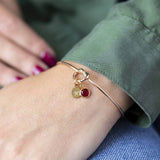 Model wears gold plated Friendship Knot Bangle with a small disc initial charm with the letter 'N' and a small garnet Swarovski birthstone charm for the month of January..