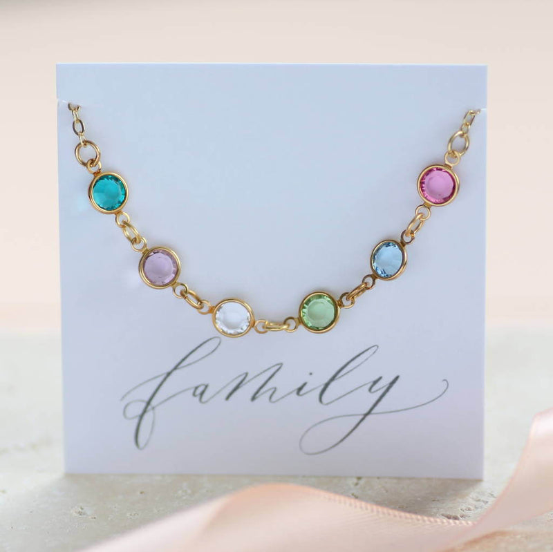 Image shows gold family swarovski birthstone link bracelet. Birthstones from left to right: December blue zircon, June light amethyst, April crystal, August peridot, March aquamarine and october rose. Bracelet is on the 'family' sentiment card.