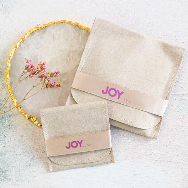 Image shows JOY by Corrine Smith branded suedette pouches in two sizes with branding in purple on a gorgeous ribbon fastening. Sitting on a white backdrop.