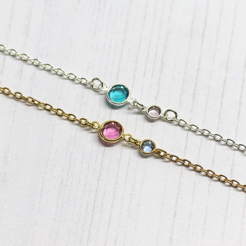 Image shows one sterling silver and one gold plated Three Generations Birthstone Bracelet sitting on a white background. Silver bracelet has December blue zircon birthstone and June light amethyst birthstone for the child. Gold bracelet shows October Rose for mother and March aquamarine for the child.