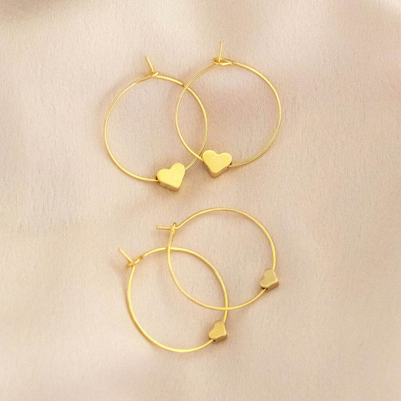 Image shows tiny gold plated heart hoop earrings on a beige backdrop. Top pair are 4mm, bottom pair are 6mm.