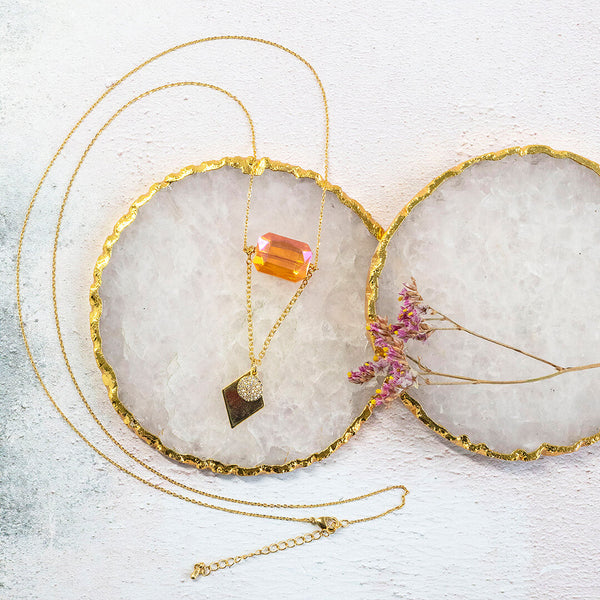 image shows apollo gold plated long length necklace featuring an orange crystal, hammered full moon and gold plated diamond shaped charm. Necklace sits on a white backdrop. 