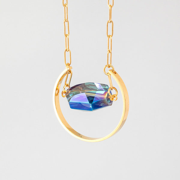 Image shows supernova blue crystal pendant necklace with blue crystal and golden arc on a grey backdrop.