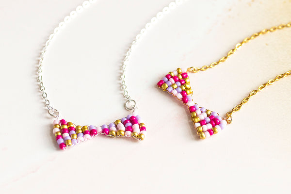 Image shows pink toned handmade beaded bow necklaces  and a yellow marbled background