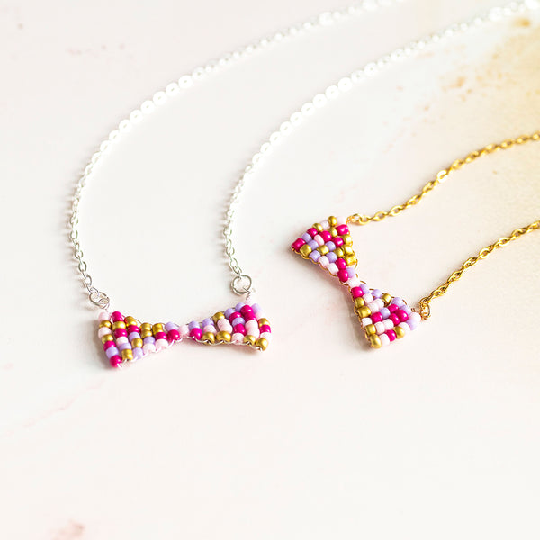 Image shows pink toned handmade beaded bow necklaces  and a yellow marbled background