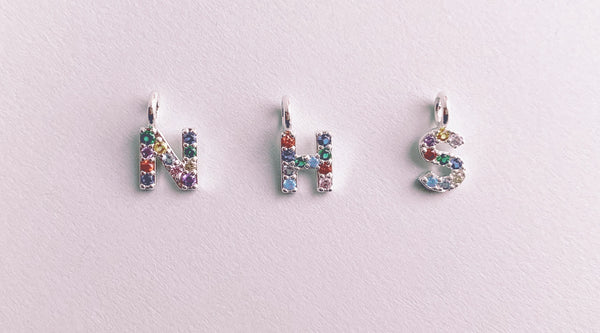 NHM spelled out in our rainbow crystal initials on silver plated brass on a light pink background.