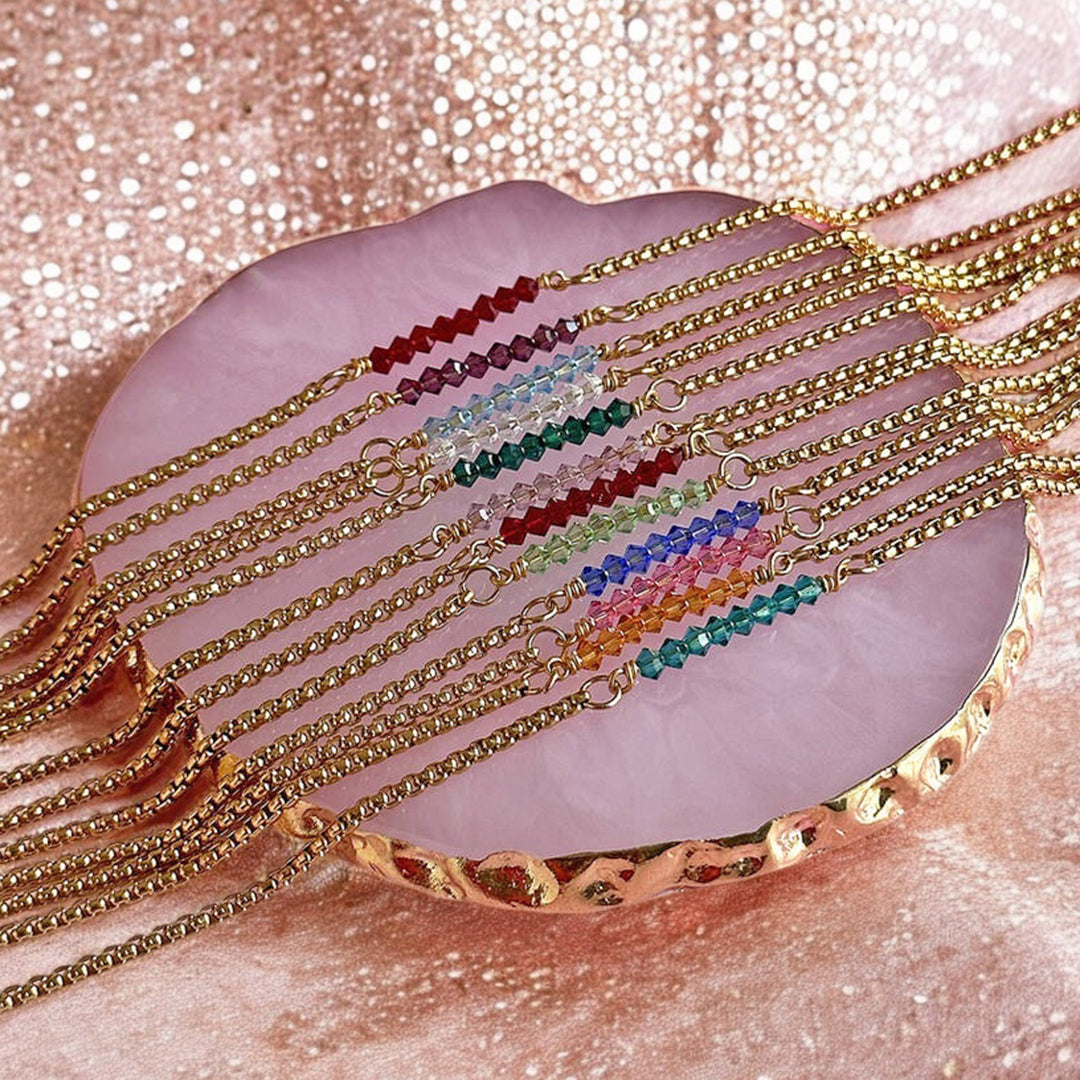 Image shows 12 gold plated tiny birthstone bar bracelets on a pink sparkly fabric surface