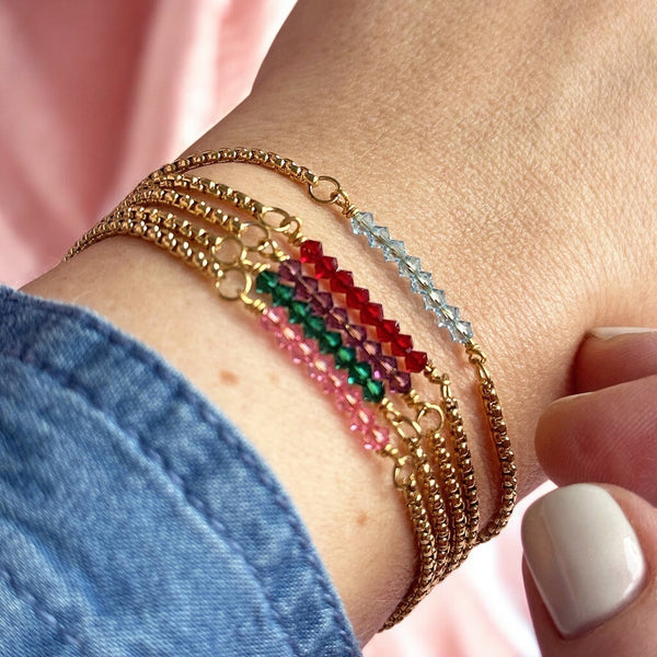 image shows a woman&#39;s wrist wearing a selection of stacked gold birthstone bar bracelets