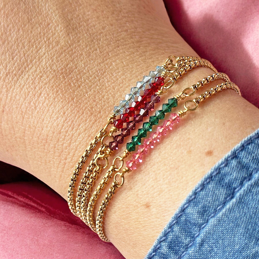 image shows a woman's wrist wearing a selection of stacked gold birthstone bar bracelets