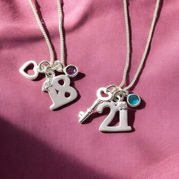 Image shows two silver charm necklaces for 18th and 21st birthday gifts on a ink background