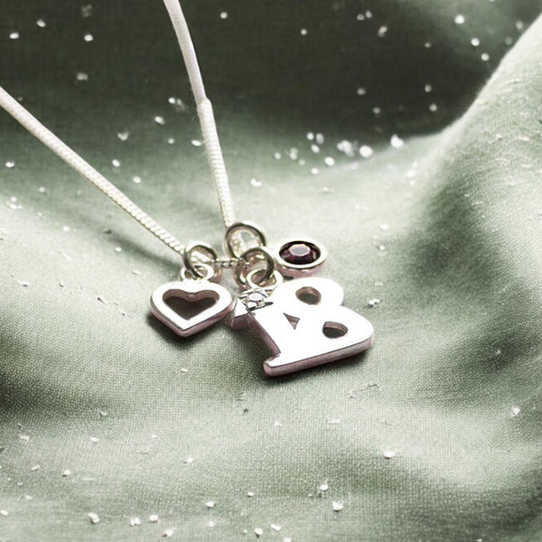 image shows a silver 18th birthday silver charm necklace with birthstone and heart charms on a green background