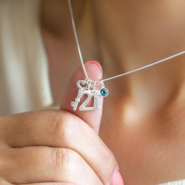 Image shows a woman wearing a silver necklace with 21 charm, birthstone charm and key charm