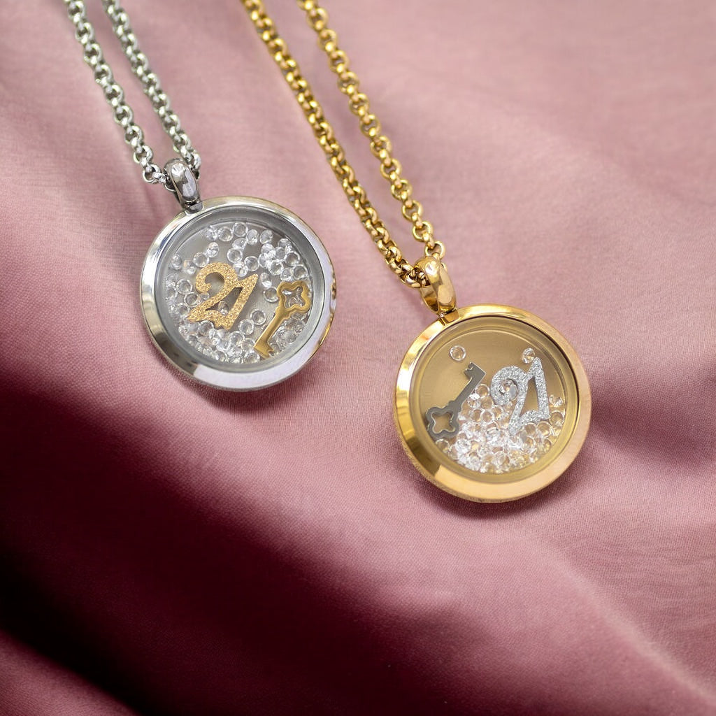 Image shows two 21st birthday locket necklaces, one in silver and one in gold on a dusky pink fabric background