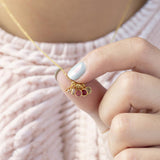 Image shows a woman holding a family birthstone necklace that she is wearing in front of a pink chunky knitted jumper