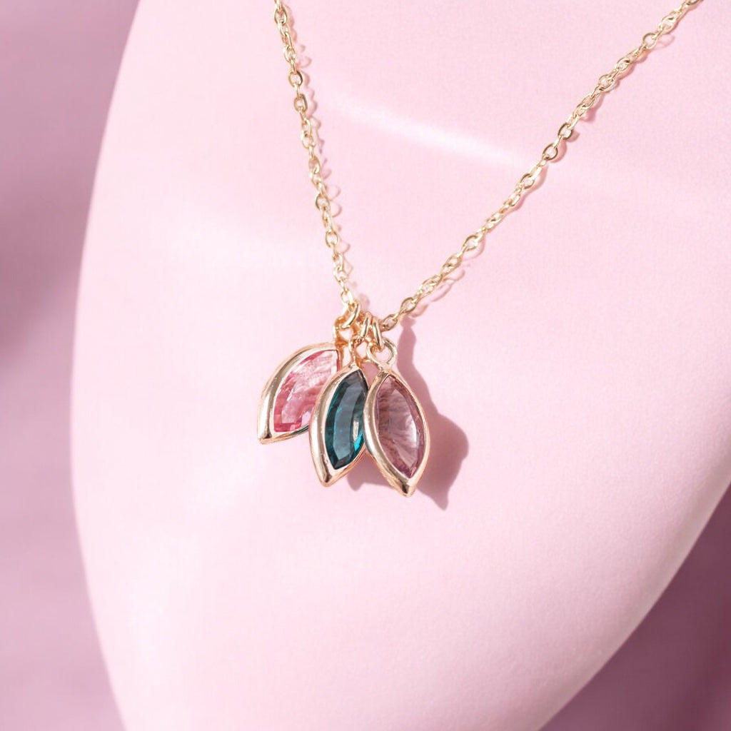 Image hows a rose gold marquise family birthstone necklace with three gemstones on a minimalist pink background