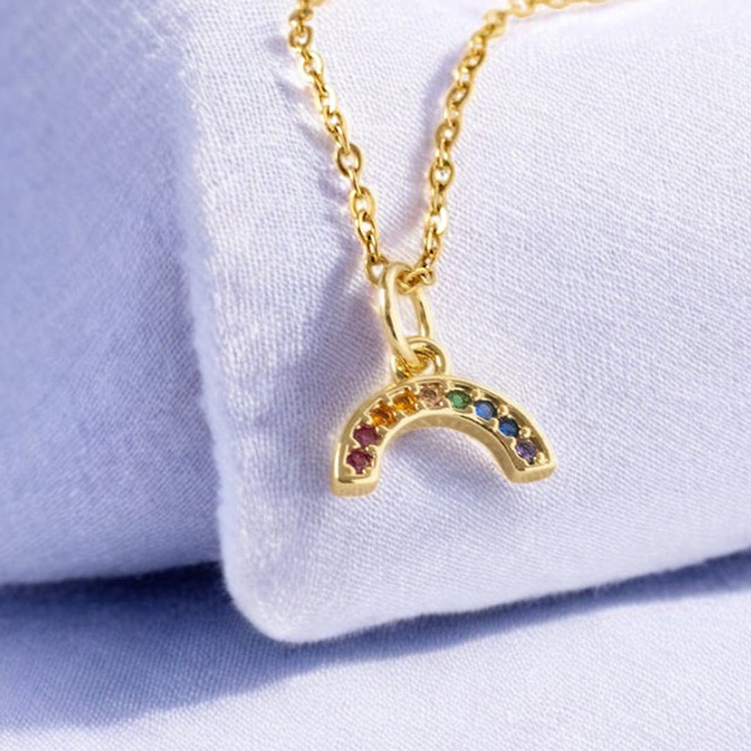 image shows a mini gold multicoloured crystal rainbow necklace on a pale blue background