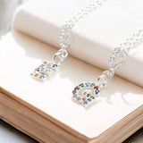 Image shows two silver necklaces with letters E and G initials that are set with multi coloured gemstones on the page of an open book