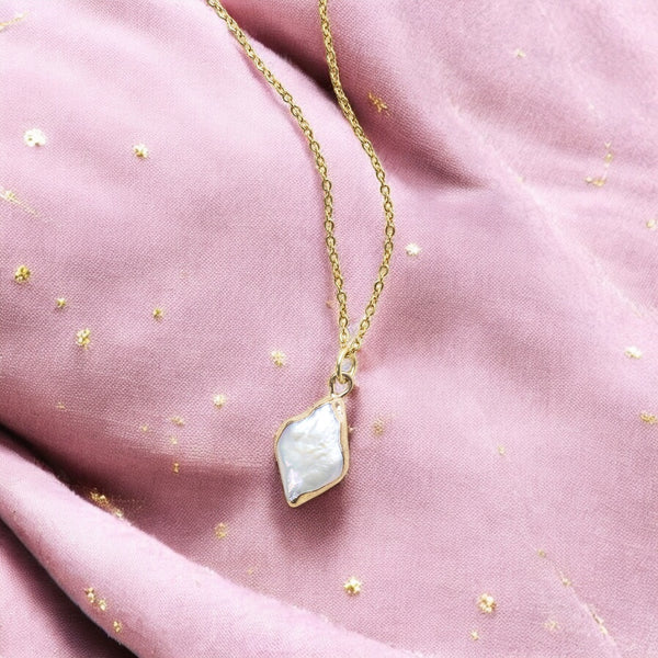 image shows gold rhombus pearl pendant necklace on a cream soft pink gold flecked background