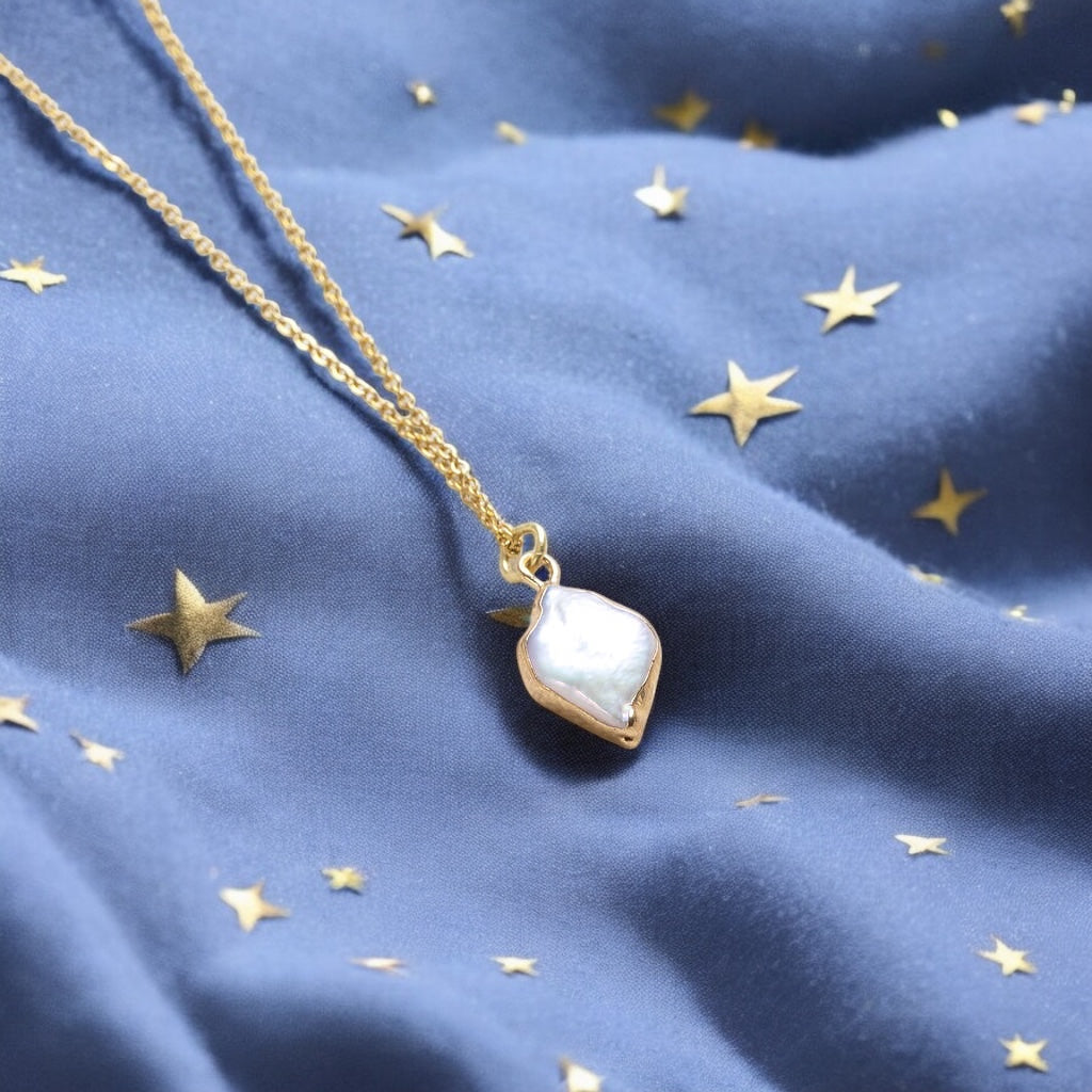 image shows gold rhombus pearl pendant necklace on a deep blue fabric background scattered with tiny gold stars 