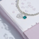 Image shows a silver beaded bracelet with a 18 number charm and a december birthstoe on a lavender notebook