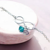 image shows a best friends infinity bracelet with thwo birthstone charms on a marble slab