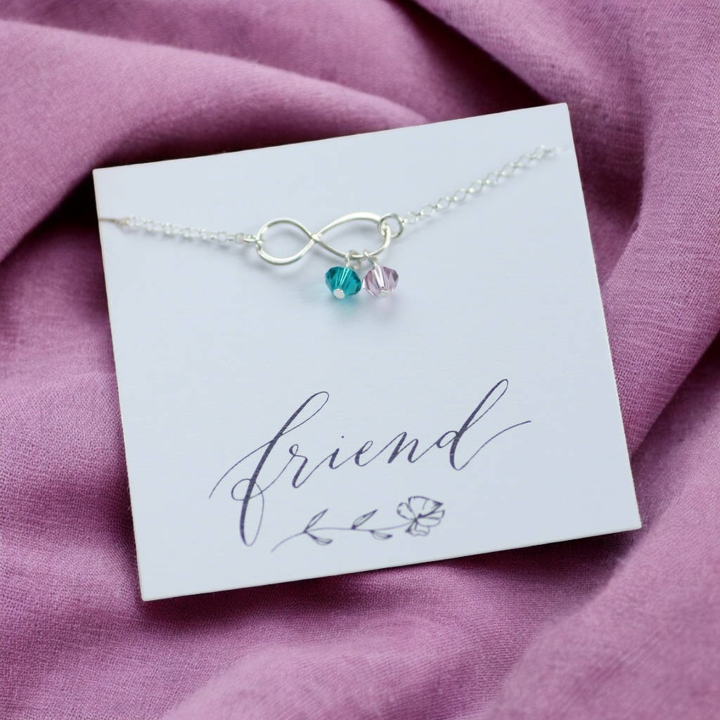 image shows a sterling silver infinity birthstone charm bracelet on a white card that says friend placed on a mauve fabric background