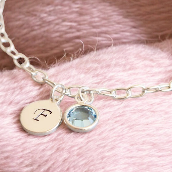 image shows a silver bracelet with handstamped F charm and aquamarine march birthstoje charm on a soft pink wool background