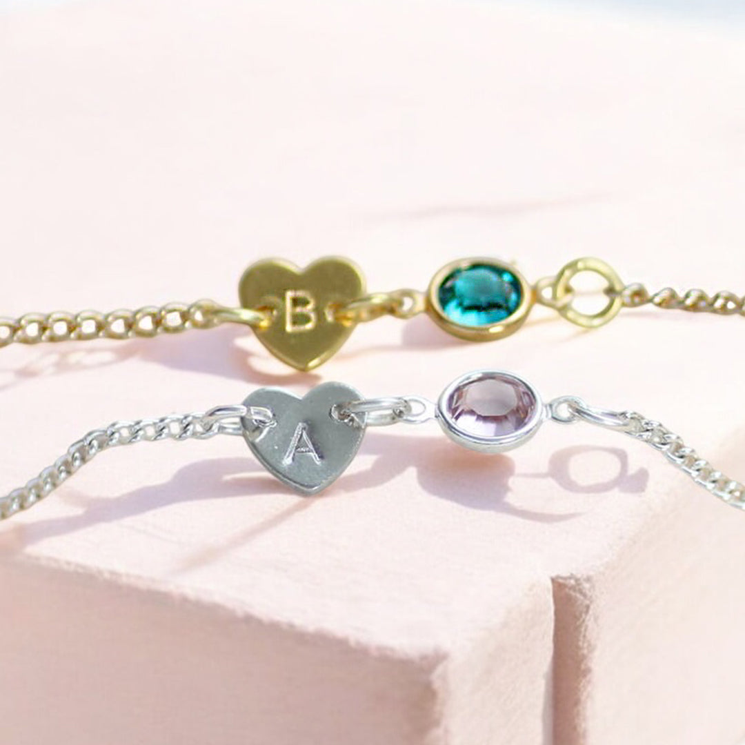 image shows two dainty heart bracelets with birthstone detail on a pale pink background