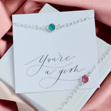 image shows two silver birthstone bracelets on a card that reads you're a gem on a dusky pink background