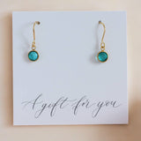 Image shows a pair of gold december birthstone earrings on a white card that reads a gift for you