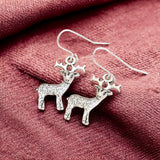 Images shows a pair of reindeer earrings on a marron fabric background