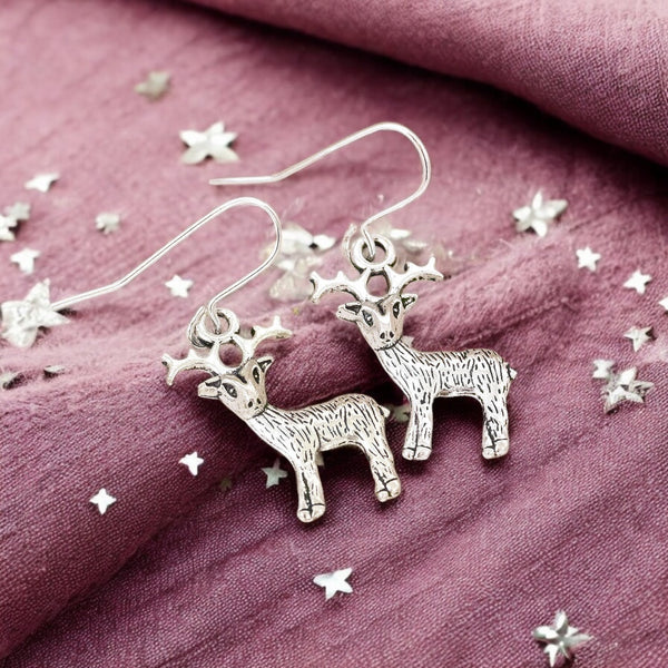 Image shows a pair of silver reindeer earrings on a maroon background with scattered silver stars