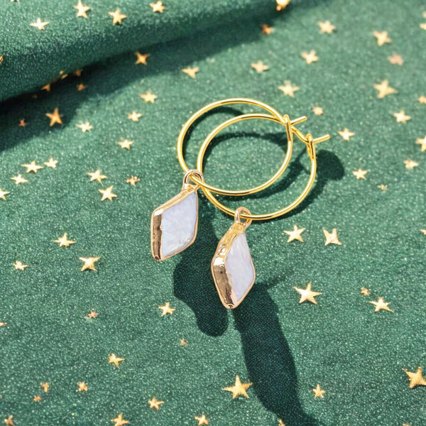 image shows a pair of gold pearl hoop earrings on a green background with gold stars