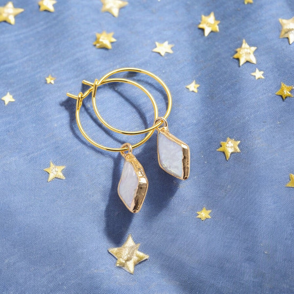 image shows a pair of gold pearl hoop earrings on a blue background with gold stars